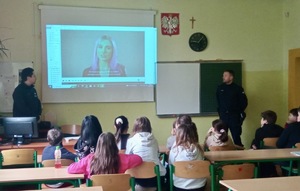 Zdjęcie przedstawia umundurowanych policjantów podczas prelekcji z uczniami. W tle prezentacja multimedialna.