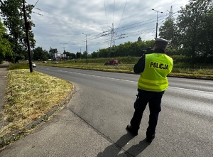 Zdjęcie przedstawia umundurowanego policjanta z wydziału ruchu drogowego mierzącego prędkość.