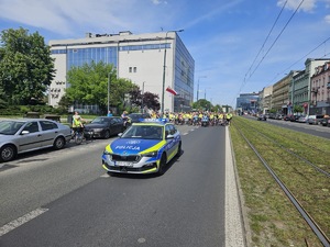 Zdjęcie przedstawia oznakowany radiowóz policyjny na drodze. Za radiowozem widoczni są uczestnicy Zagłębiowskiej Masy Krytycznej na rowerach.