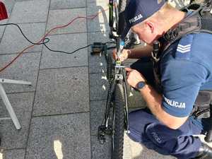 Zdjęcie przedstawia umundurowanego policjanta grawerującego rower.