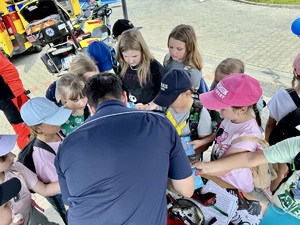 Zdjęcie przedstawia umundurowanego policjanta z grupą dzieci przy stoisku sosnowieckiej komendy.