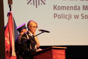 Zdjęcie przedstawia umundurowaną policjantkę przemawiającą do gości.