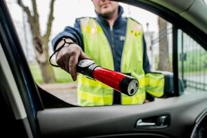 Zdjęcie przedstawia umundurowanego policjanta trzymającego w ręku alkomat.