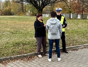 Zdjęcie przedstawia umundurowaną policjantkę  wręczającą ludziom elementy odblaskowe.