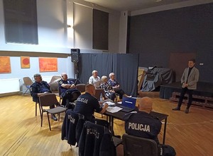 Zdjęcie przedstawia umundurowanych policjantów oraz uczestników debaty w sali.