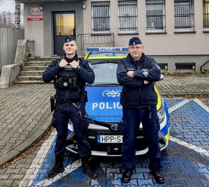 Zdjęcie przedstawia dwóch umundurowanych policjantów stojących przez komisariatem IV w Sosnowcu.