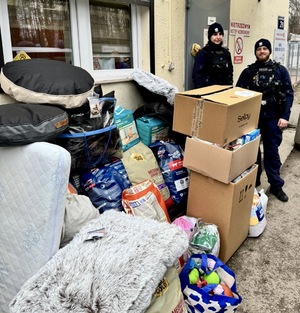 Zdjęcie przedstawia policjantkę i policjanta stojących obok darów przekazanych dla schroniska dla zwierząt w Sosnowcu.