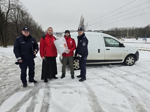 Zdjęcie przedstawia mężczyznę, księdza i dwóch umundurowanych policjantów przy samochodzie z paczką.