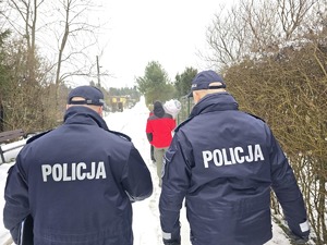 Zdjęcie przedstawia dwóch umundurowanych policjantów oraz mężczyznę z paczką idących drogą.