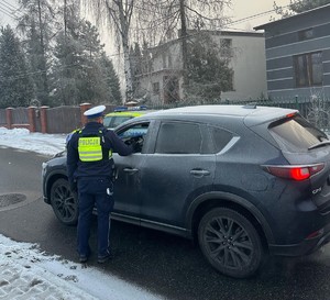 Zdjęcie przedstawia umundurowanego policjanta wydziału ruchu drogowego sprawdzającego trzeźwość kierowcy.