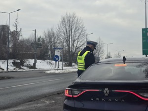 Zdjęcie przedstawia umundurowanego policjanta z wydziału ruchu drogowego przy samochodzie podczas działań.