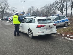 Zdjęcie przedstawia mundurowego z sosnowieckiej drogówki oraz biały samochód marki Volkswagen.