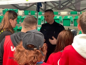 Zdjęcie przedstawia umundurowanego policjanta rozmawiającego z grupą młodzieży.