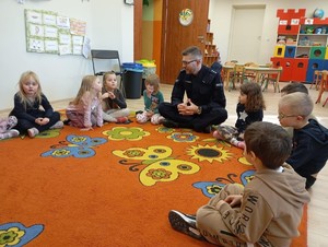 Zdjęcie przedstawia umundurowanego policjanta z grupą dzieci siedzących na podłodze.