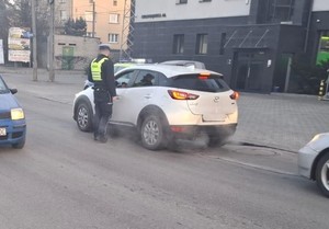 Zdjęcie przedstawia umundurowanego policjanta sprawdzającego trzeźwość kierowcy samochodu na ulicy.