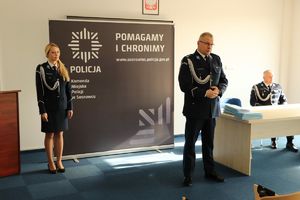 Zdjęcie przedstawia Komendanta Miejskiego Policji w Sosnowcu oraz Pierwszego Zastępcę Komendanta Miejskiego Policji w Sosnowcu, umundurowaną policjantkę na tle roll-upu podczas uroczystości.