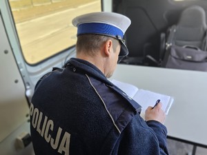 Zdjęcie przedstawia umundurowanego policjanta ruchu drogowego piszącego w notatniku.