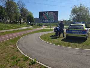 Zdjęcie przedstawia umundurowanego policjanta oraz oznakowany radiowóz i motocykl służbowy.