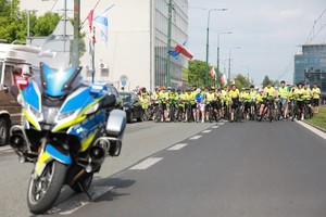 Zdjęcie przedstawia motocykl policyjny. W tle uczestnicy wydarzenia na rowerach w kamizelkach odblaskowych.