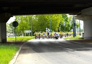 Zdjęcie przedstawia policjanta na motocyklu służbowym. Za nim poruszają się uczestnicy wydarzenia na rowerach w kamizelkach odblaskowych.
