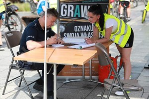 Zdjęcie przedstawia umundurowanego policjanta oraz uczestniczkę wydarzenia. W tle plakat promujący akcję &amp;quot;Grawer&amp;quot;.