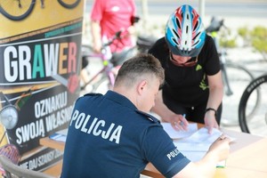 Zdjęcie przedstawia umundurowanego policjanta oraz uczestniczkę wydarzenia. W tle plakat promujący akcję &amp;quot;Grawer&amp;quot;.