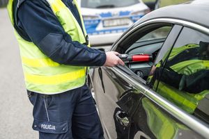 Zdjęcie przedstawia umundurowanego policjanta badającego trzeźwość kierującego.