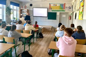 Zdjęcie przedstawia umundurowanego policjanta podczas prelekcji. W sali znajdują się uczniowie.
