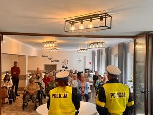 Zdjęcie przedstawia umundurowaną policjantkę oraz policjanta podczas spotkania z seniorami w sali.