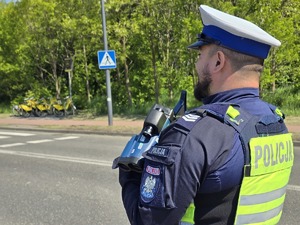Zdjęcie przedstawia umundurowanego policjanta wydziału ruchu drogowego. W tle przejście dla pieszych.