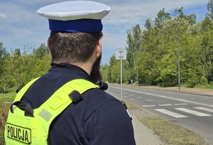 Zdjęcie przedstawia umundurowanego policjanta wydziału ruchu drogowego. W tle przejście dla pieszych.