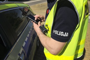 Zdjęcie przedstawia umundurowanego policjanta wydziału ruchu drogowego podczas działań oraz radiowóz.