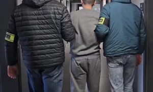 Zdjęcie przedstawia nieumundurowanych policjantów z opaskami z napisem &quot;Policja&quot; z zatrzymanym&quot;.