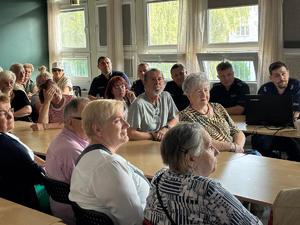 Zdjęcie przedstawia uczestników debaty siedzących przy stole oraz umundurowanych policjantów.