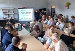 Zdjęcie przedstawia uczestników debaty siedzących przy stole oraz umundurowanych policjantów.