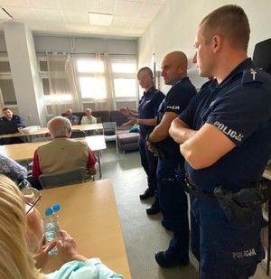 Zdjęcie przedstawia uczestników debaty siedzących przy stole oraz umundurowanych policjantów.