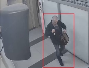 Zdjęcie przedstawia wychodzącego z pomieszczenia mężczyznę z szarej koszulce, z plecakiem w ręku.