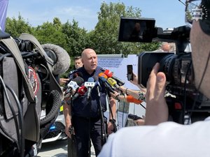 Zdjęcie przedstawia umundurowanego policjanta odpowiadającego na pytania dziennikarzy.