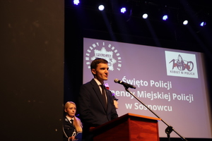 Zdjęcie przedstawia mężczyznę przemawiającego ze sceny.