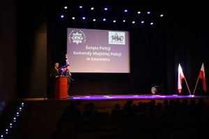 Zdjęcie przedstawia mężczyznę przemawiającego ze sceny.