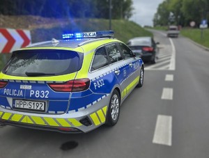 Zdjęcie przedstawia policyjny, oznakowany radiowóz oraz pojazd.