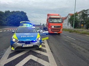 Zdjęcie przedstawia policyjny, oznakowany radiowóz oraz pojazd.