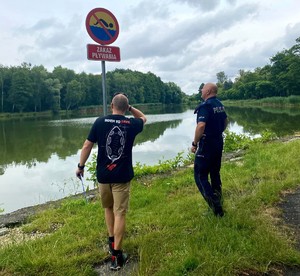 Zdjęcie przedstawia umundurowanego policjanta oraz przedstawiciela WOPR podczas kontroli zbiorników wodnych.