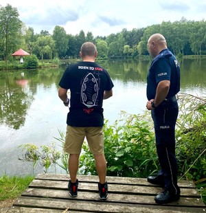 Zdjęcie przedstawia umundurowanego policjanta oraz przedstawiciela WOPR podczas kontroli zbiorników wodnych.