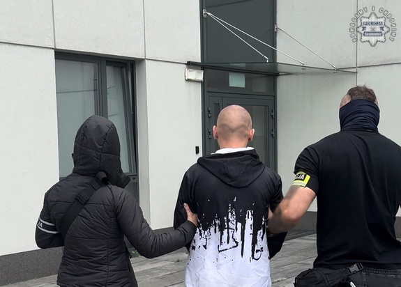 Zdjęcie przedstawia nieumundurowanych policjantów prowadzących osobę zatrzymaną do jednostki policji.
