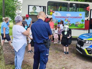 Zdjęcie przedstawia umundurowanego policjanta oraz uczestników Mopsikobusa.