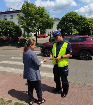 Zdjęcie przedstawia umundurowanego policjanta wręczającego kobiecie element odblaskowy.