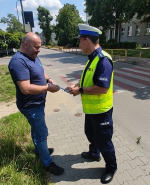 Zdjęcie przedstawia umundurowanego policjanta wręczającego mężczyźnie element odblaskowy.
