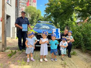 Zdjęcie przedstawia umundurowaną policjantkę i policjanta oraz dzieci na tle radiowozu.