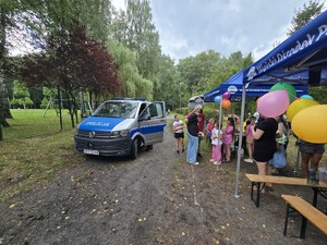 Zdjęcie przedstawia oznakowany radiowóz służbowy oraz grupę dzieci.